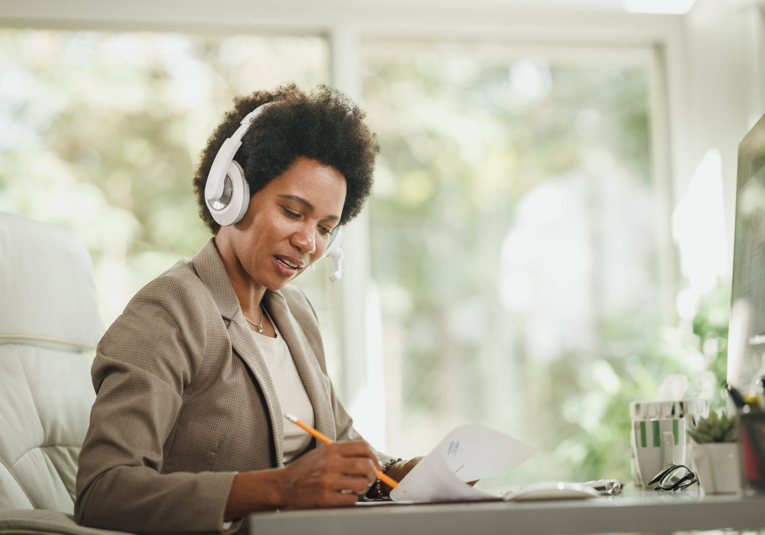 Shot of an African woman wearing a headphones and working at her desk during corona virus pandemic.