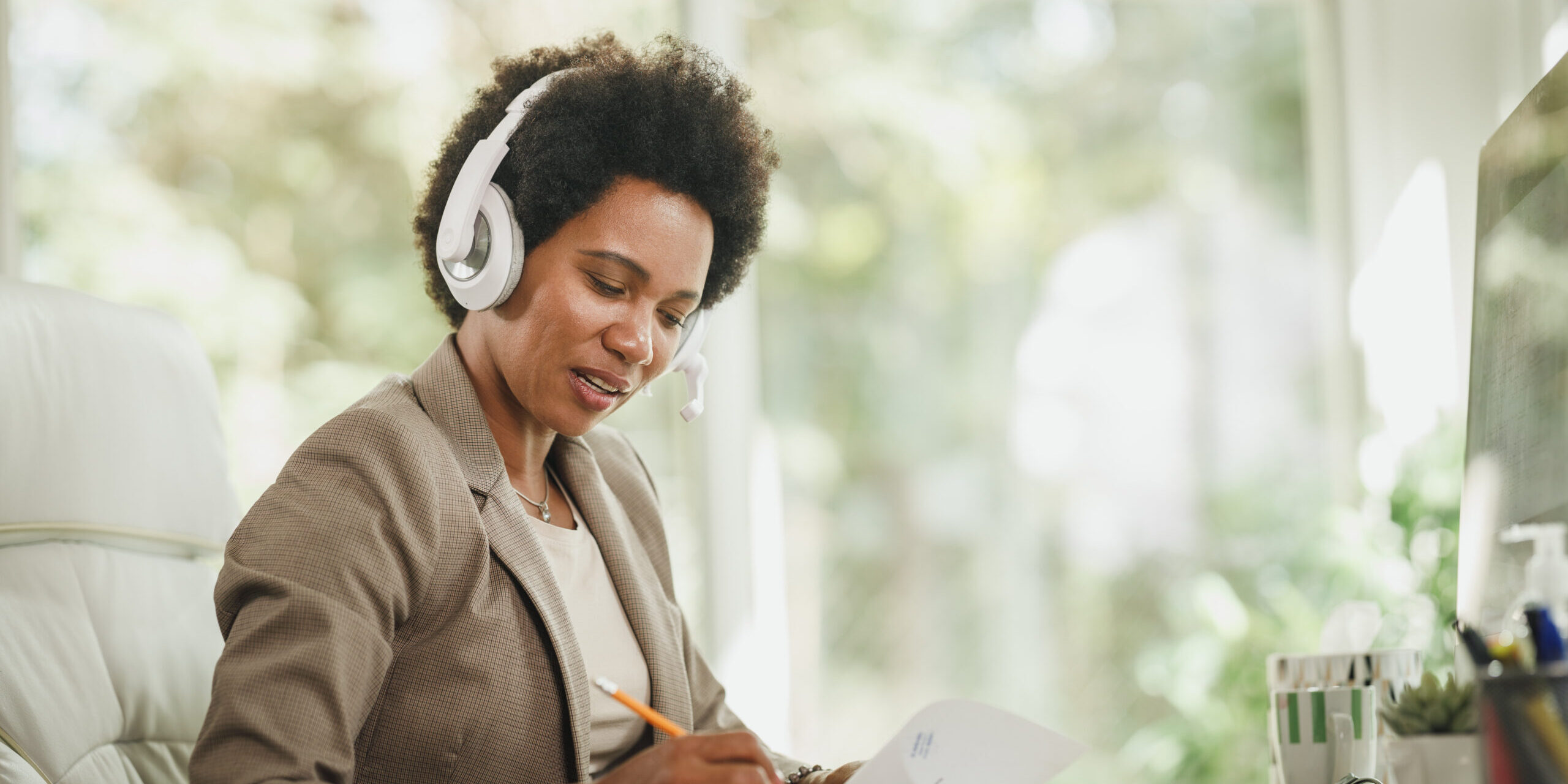 Shot of an African woman wearing a headphones and working at her desk during corona virus pandemic.