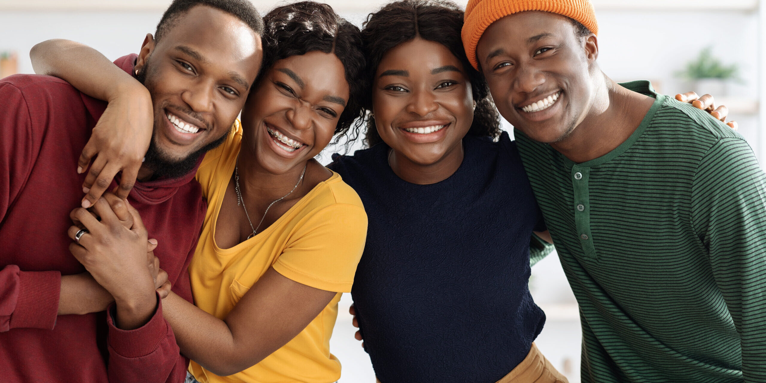 Portrait of cheerful african american millennial couples, living room interior, cute black guys and ladies in casual having double date at home, hugging and smiling at camera, closeup